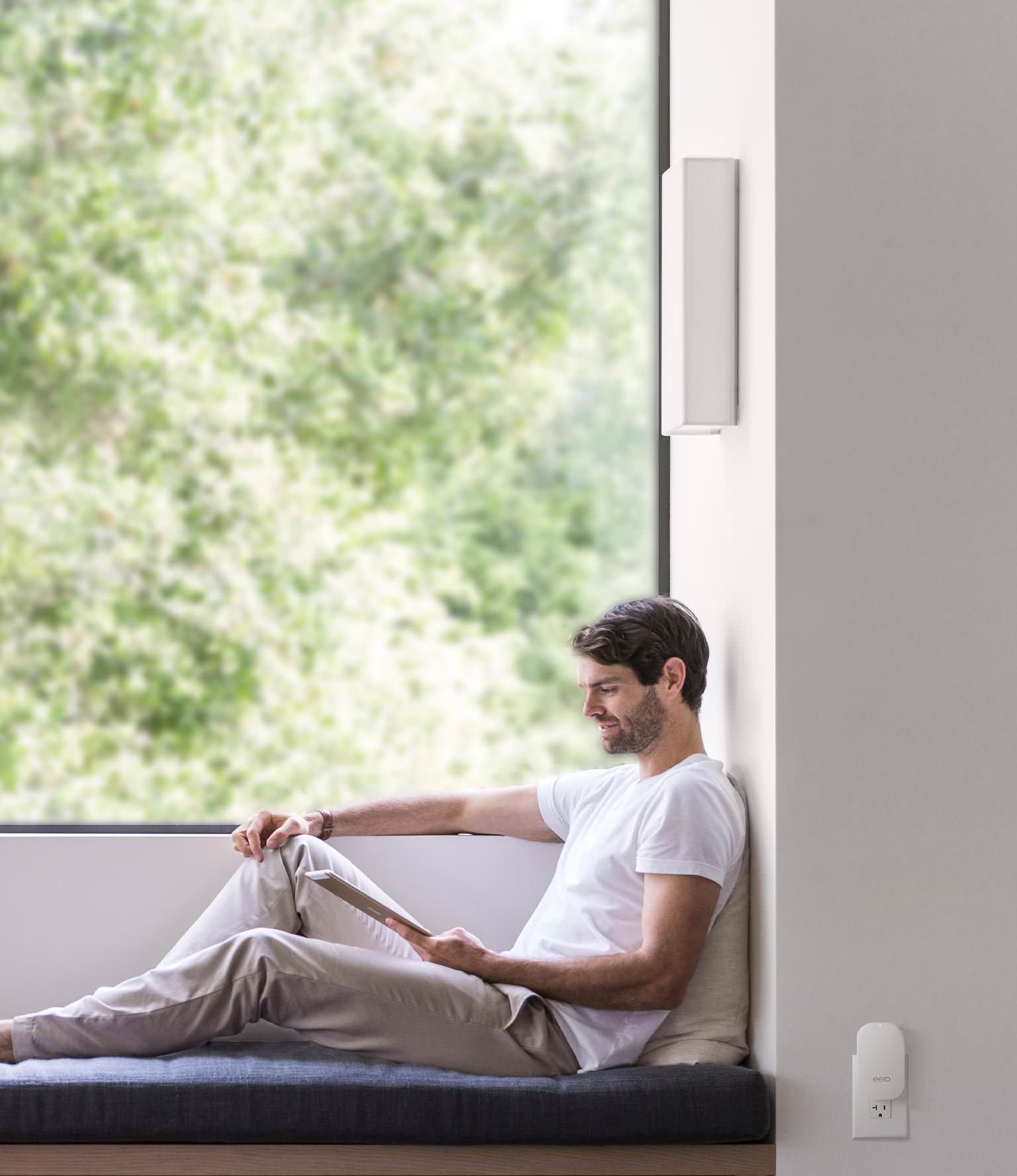 Man relaxing while using an iPad. An eero Beacon is nearby on the wall.