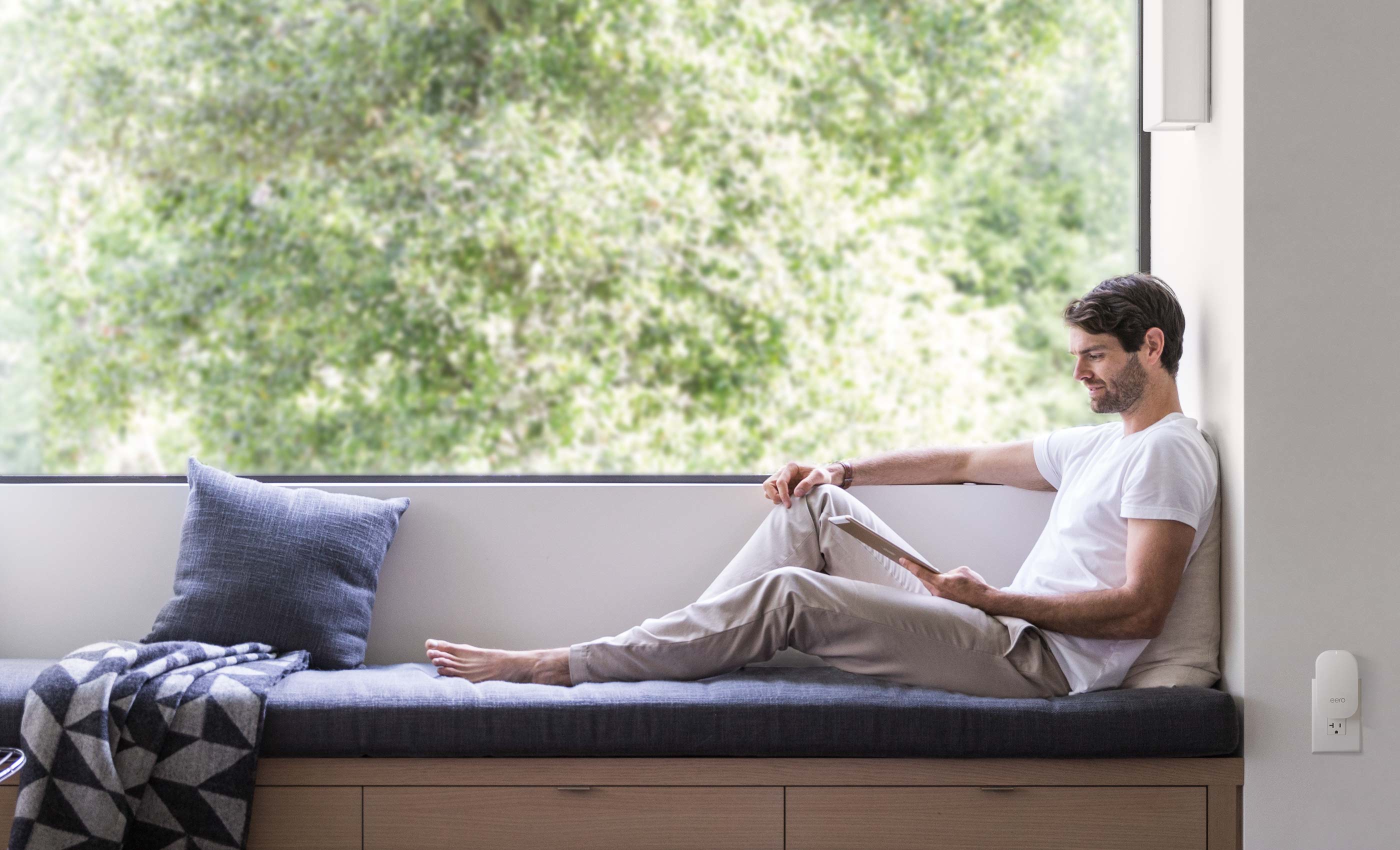 Man relaxing while using an iPad. An eero Beacon is nearby on the wall.